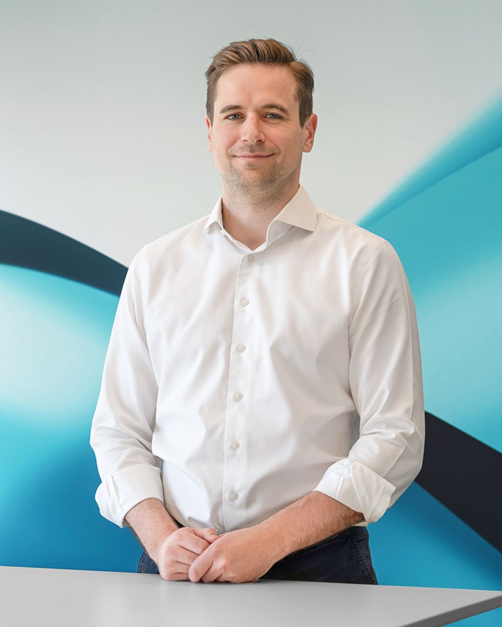 Philipp Lassernig wearing a white dress shirt, standing with hands clasped, in front of a modern, abstract TRATON background.