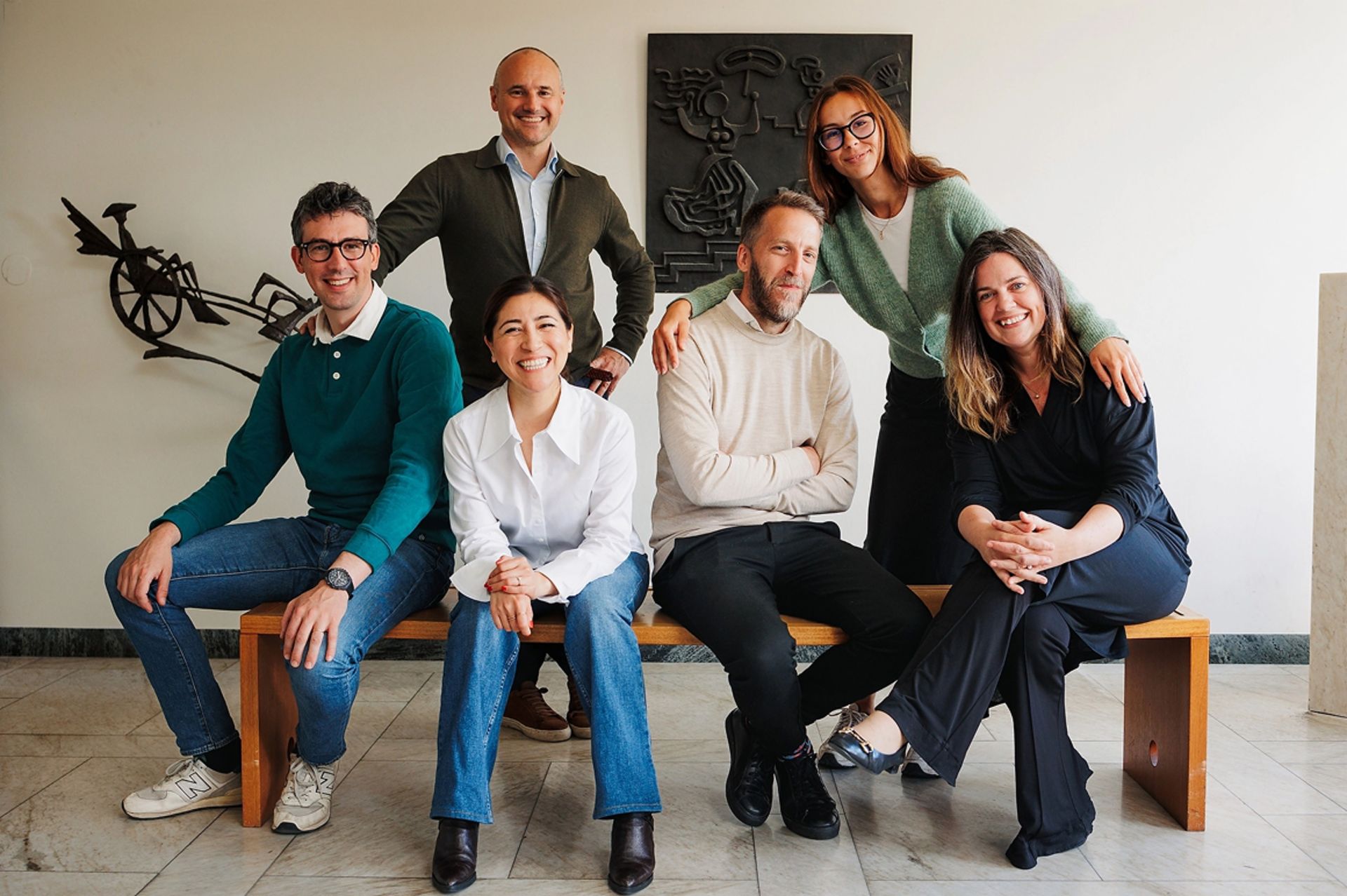 Six TRATON employees of various genders and ethnicities sitting and standing in front of a wall with artwork
