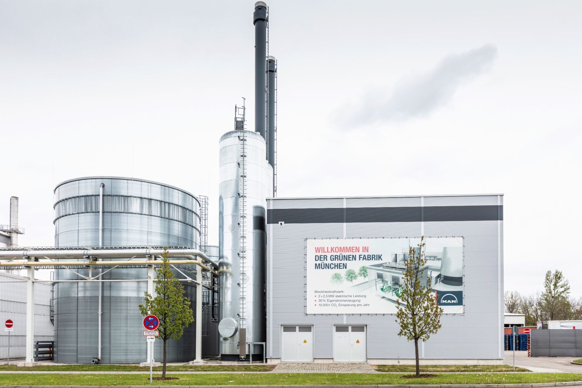 Exterior view of the Green Factory Munich, featuring industrial buildings and a sign highlighting its eco-friendly initiatives.