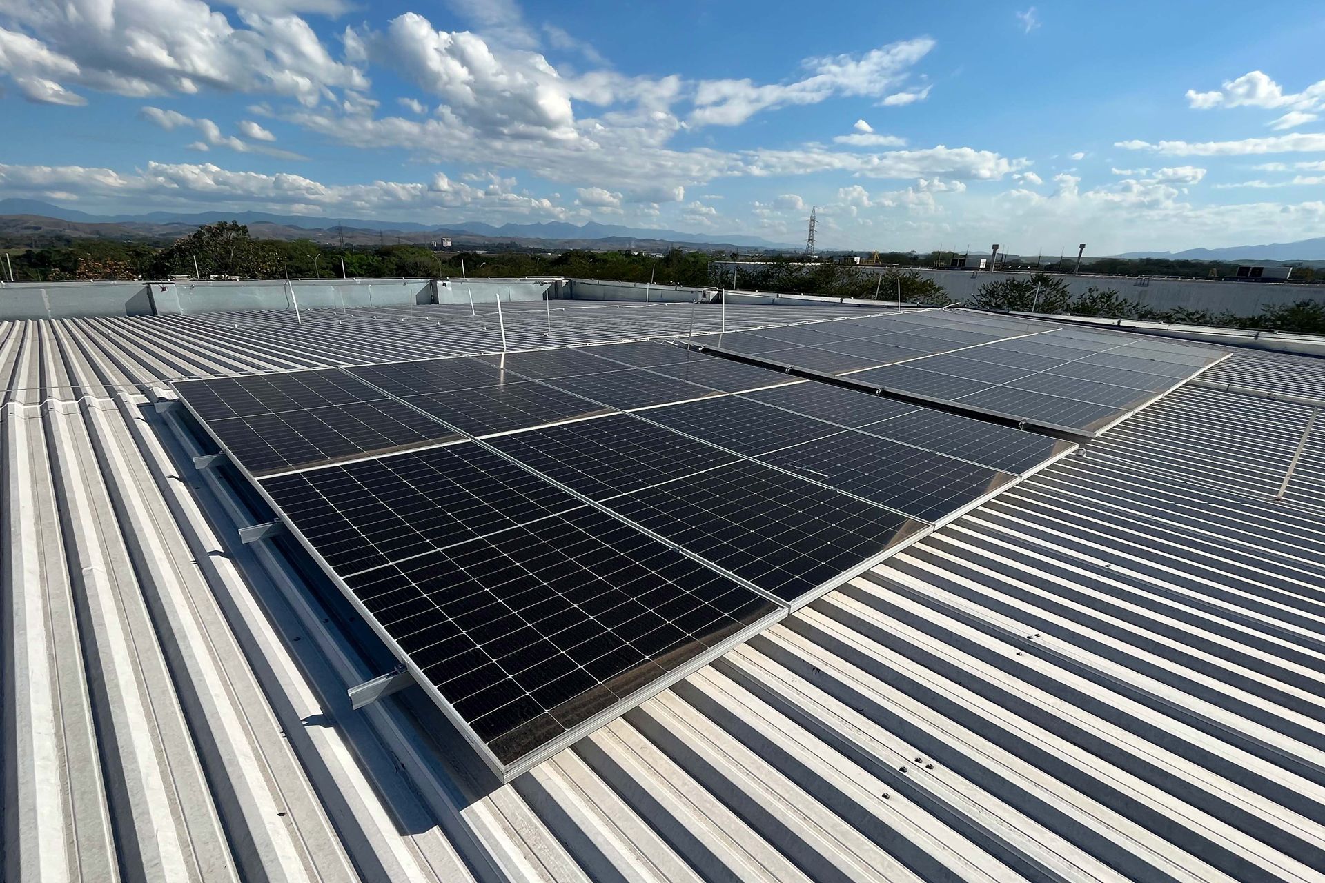 Solar panels installed on a metal rooftop under a clear blue sky, surrounded by a scenic landscape.