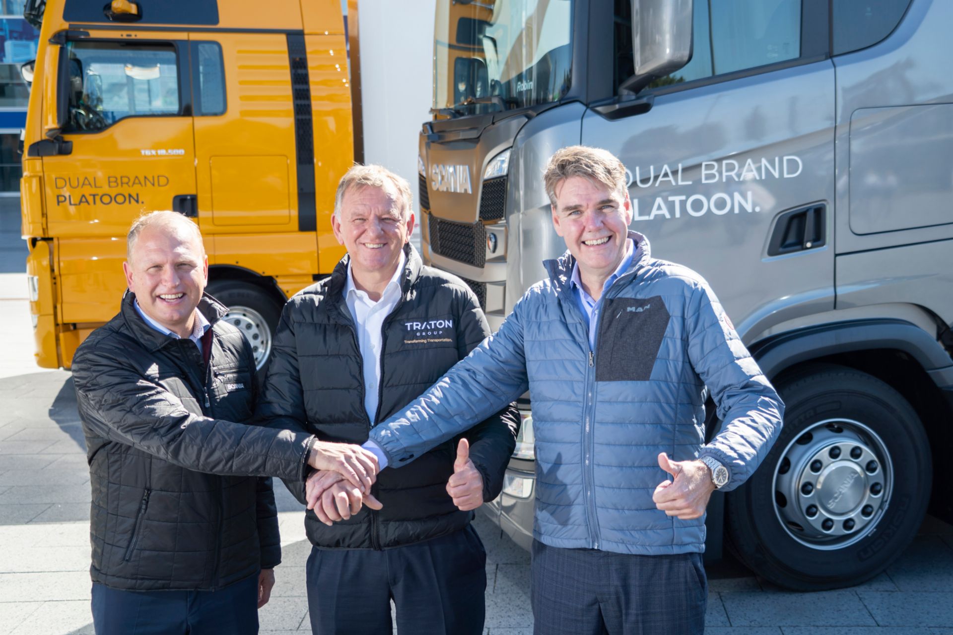 Henrik Henriksson, Andreas Renschler and Joachim Drees look smilingly into the camera and shake hands.