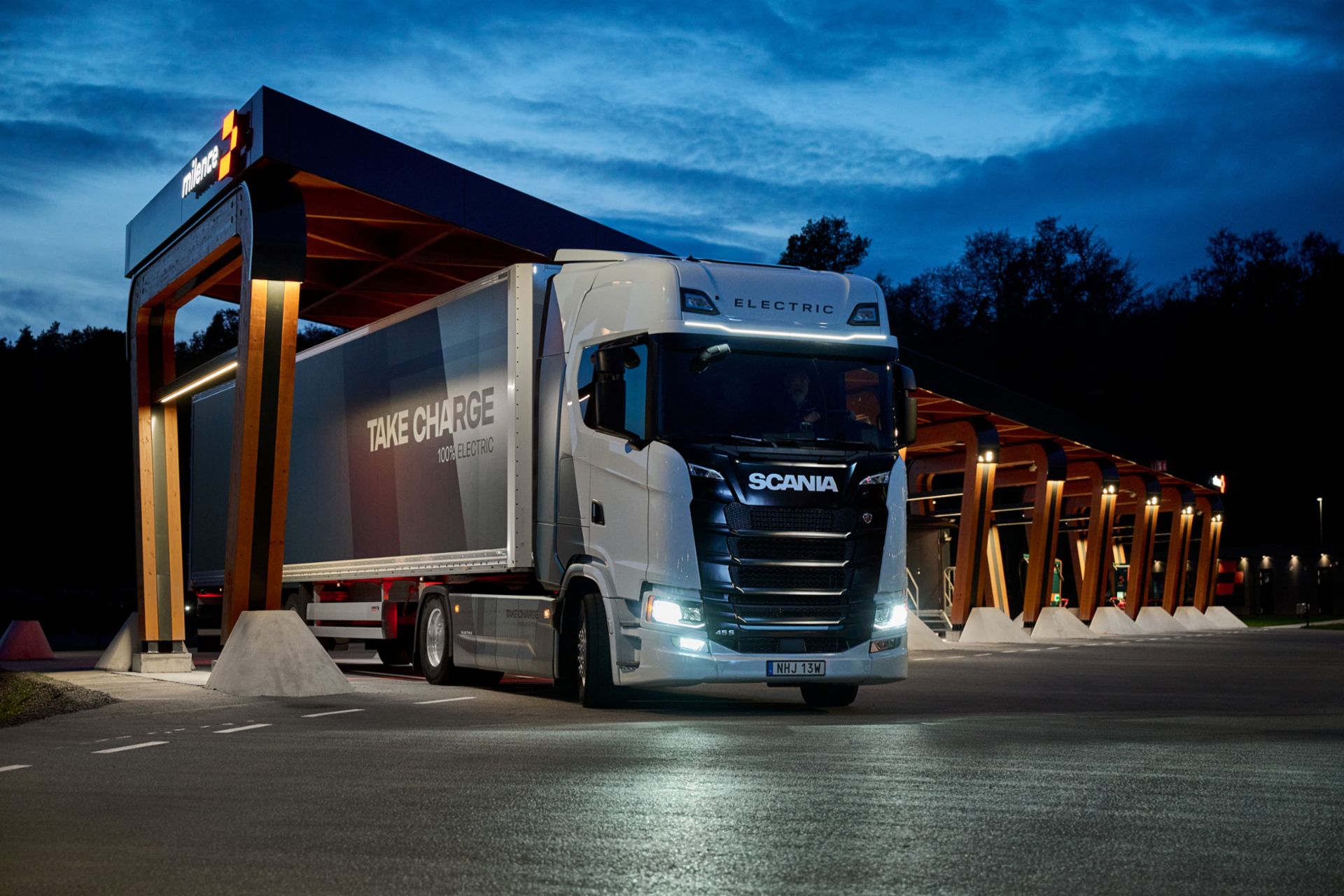 Scania Elektro-Lkw beim Laden an einer beleuchteten Milence-Ladestation in der Dämmerung